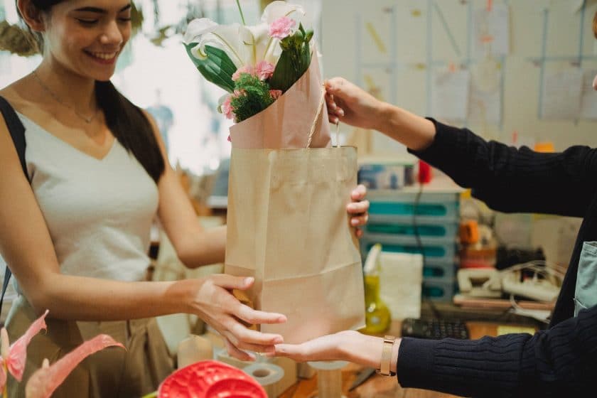 Imagem de uma cliente satisfeita recebendo um pacote de compras com flores.