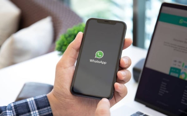 Mãos segurando um telefone com a logomarca do WhatsApp na tela, simulando uma das etapas do fluxo de atendimento.