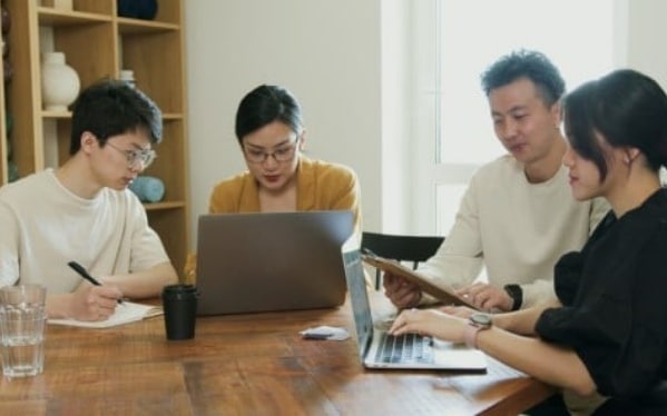 Pessoas reunidas em volta da mesa de reuniões com seus computadores e cadernetas para discutirem sobre o fluxo de atendimento